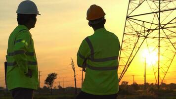 silueta de ingeniero equipos mirando que se discute plan. dos ingeniero en pie en campo con electricidad torres a puesta de sol. foto