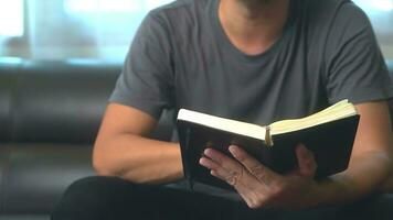 close-up young asian man reading a book or novel while relaxing on a sofa in his minimal living room. photo