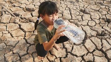 Rural girl with sitting drinking clean water on dry ground. Concept drought and crisis environment. photo