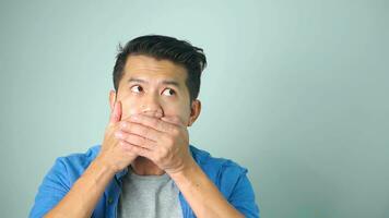 Asian man confused shocked close mouth with hands from unexpected bad news failure crime covers lips oops say terrible secret keep silence. photo