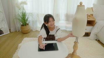 asiático joven niña utilizar tableta a encontrar referencia a diseño ropa en dormitorio. foto