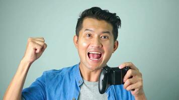 Happy face of Asian gamer holding joystick playing video game online at while background. photo