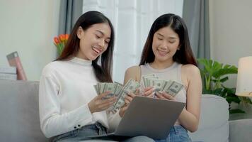 Two asian girls counting money dollars at home. Online business success consept. photo