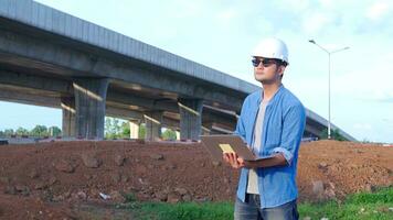 Asian civil engineer using laptop is inspecting construction project a road expressway that is done at construction site. photo