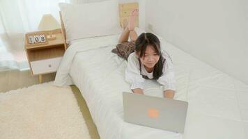 Happy little girl child. Cute little girl lie on his stomach a bed and watching something interesting on a laptop. photo