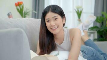 hermosa asiático joven mujer leyendo libro en sofá a hogar. foto