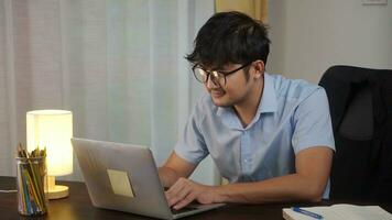 asiático hombre sonriente trabajando en línea con ordenador portátil a hogar oficina, teletrabajo concepto. foto