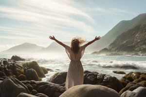 A young woman with outstretched arms enjoying the wind and breathing fresh air on the rocky beach , sunset , Generative AI. photo