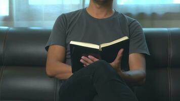 close-up young asian man reading a book or novel while relaxing on a sofa in his minimal living room. photo