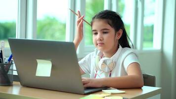 Kid girl learns lessons, thoughtful child doing homework thoughtfully looking to a laptop screen . Remote education technologies and homework. photo