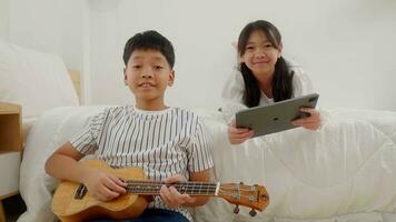 A girl lying in bed playing tablet and a boy sitting beside bed playing guitar in a bedroom. photo