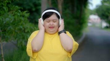 Happy asian girl with down syndrome in headphones and sing while exercising in the park. photo