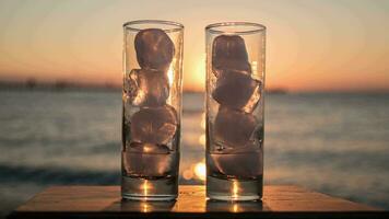 Glasses with melting ice against sea and sunset background video