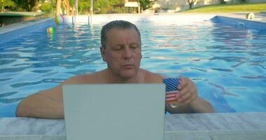 sorridente uomo nel casa piscina con il computer portatile video