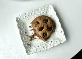 Chocolate chip cookie on a white plate with a golden spoon on white wooden table, top view photo