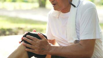 Senior asian active man has knee injury accident at trees park during. He using hands massage legs to relieve pain.Tendon and muscle problems. photo