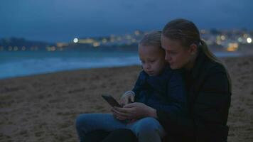 Mother and daughter watching something on smartphone at ocean beach video