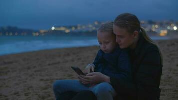 moeder en dochter aan het kijken iets Aan smartphone Bij oceaan strand video