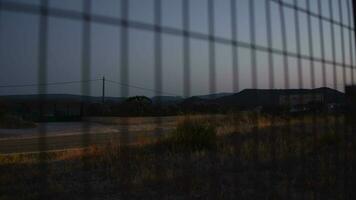 Looking at country road in the dusk through wire metal fence video