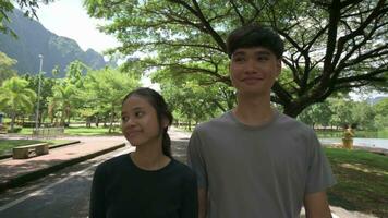 Two asian young teenagers in casual dress walking and talking together on the street in nature park. video