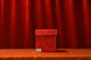 A red box with a red envelope on a table in front of a red curtain photo