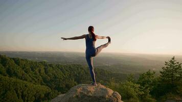 Atlético mulher fazendo ioga poses em topo do uma montanha durante pôr do sol. Esportes menina trens e faz alongamento exercícios dentro a montanhas. saudável estilo de vida, zenismo, exercite-se conceito. lento movimento. video