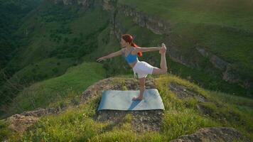 Atlético mulher fazendo ioga poses em topo do uma montanha durante pôr do sol. Esportes menina trens e faz alongamento exercícios dentro a montanhas. saudável estilo de vida, zenismo, exercite-se conceito. lento movimento. video