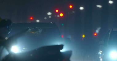 Car with dazzle lights moving slowly in night city under the rain video