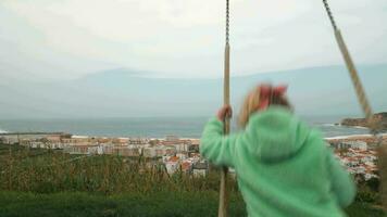 Little girl looking at ocean and resort town from the swing. Nazare in Portugal video