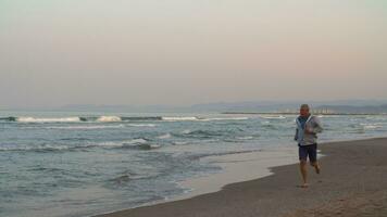 retraité homme le jogging sur le plage à le coucher du soleil video