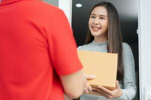 Happy smiling woman receives boxes parcel from courier in front house. Delivery man send deliver express. online shopping, paper containers, takeaway, postman, delivery service, packages photo