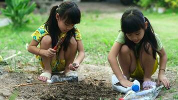weinig meisje aanplant planten in potten van gerecycled water flessen in de achtertuin. recycle water fles pot, tuinieren activiteiten voor kinderen. recycling van plastic verspilling video