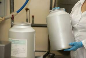 Gloved hands hold a metal container in a veterinary drug manufacturing plant. photo