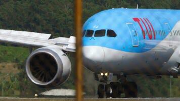 PHUKET, THAILAND JANUARY 22, 2023 - Commercial plane Boeing 787 of TUI Fly taxiing at Phuket airport. Flaps up when braking. Runway end, view through the fence. Travel concept video