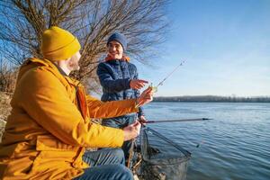 Father and son are fishing on sunny winter day. Freshwater fishing. Teenage boy is learning to fish. photo