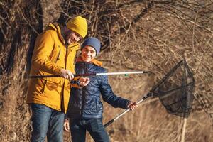 padre y hijo son pescar en soleado invierno día. agua dulce pesca. Adolescente chico es aprendizaje a pez. foto