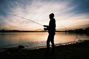 Teenage boy is fishing on river bank. Boy is fishing in sunset. photo