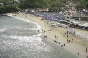 Aerial drone view of Holiday In Ndrini Beach, Yogyakarta, Indonesia with ocean, beach, umbrellas, and people. photo