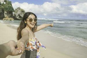 A happy young Asian woman is smiling to the camera and pointing at the beach in Gunungkidul, Indonesia. photo