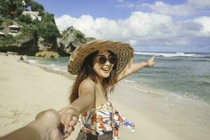 A happy young Asian woman is smiling to the camera and pointing at the beach in Gunungkidul, Indonesia. photo