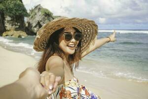 un contento joven asiático mujer es sonriente a el cámara y señalando a el playa en gunungkidul, Indonesia. foto