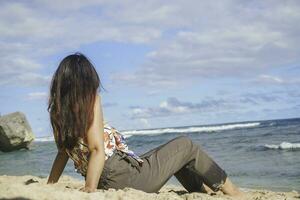 Young Asian woman sit on the beach sand. Portrait sexy Asian lady traveling and relaxing in the summer with tropical nature. photo