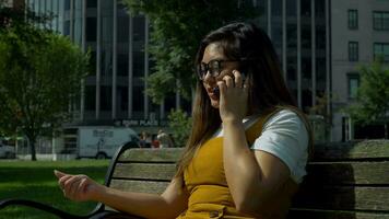 4k Woman in the Summer Heat Sits on a Bench and Talks to her family on the phone video