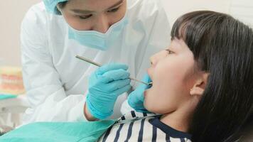 asiatisk kvinna pediatrisk tandläkare checkar och undersöker en liten flickans tänder, förklarade förbi implantera modell i dental klinik, välbefinnande hygien, och professionell ortodontisk sjukvård i unge sjukhus. video