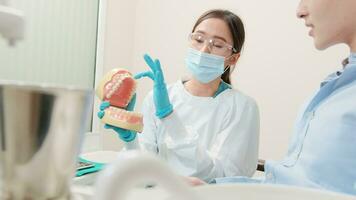 asiatisk kvinna tandläkare förklara ortodontisk vård och blekning till ung manlig patient med tänder modell i dental klinik, välbefinnande hygien, och professionell sjukvård arbete i läkare kontor sjukhus. video