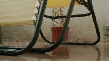 A yellow chair and a flower are getting wet on the balcony in the rain video