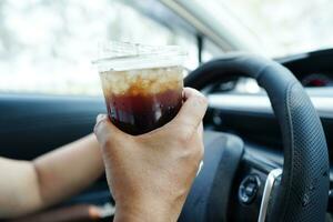 Asian woman driver hold drink in car, dangerous and risk an accident. photo