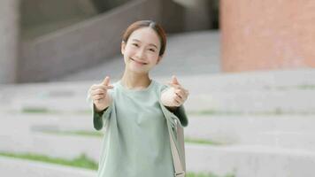 mignonne asiatique fille dans Facile manteau montrant coréen cœur avec doigt et en riant sourire. video