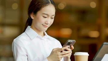 Asian woman sitting and typing messages in front of a coffee shop video