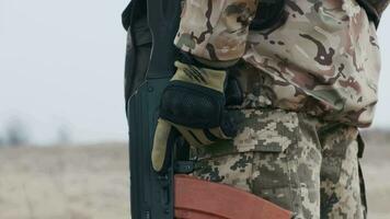 professionnel soldat avec arme dans militaire uniforme des stands sur garde avec l'automne champ et gris ciel dans Contexte. troupe sur le barrage routier. combattant dans plein munition. concept de guerre video